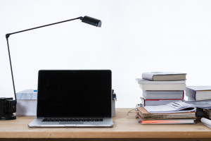 Foto mit einem Ordentlichen Schreibtich, mit einem aufgeklappten Laptop, einer Schreibtischlampe und Büchern