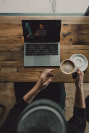 Foto mit einer Person vor einem Laptop und einer Kaffeetasse in der Hand