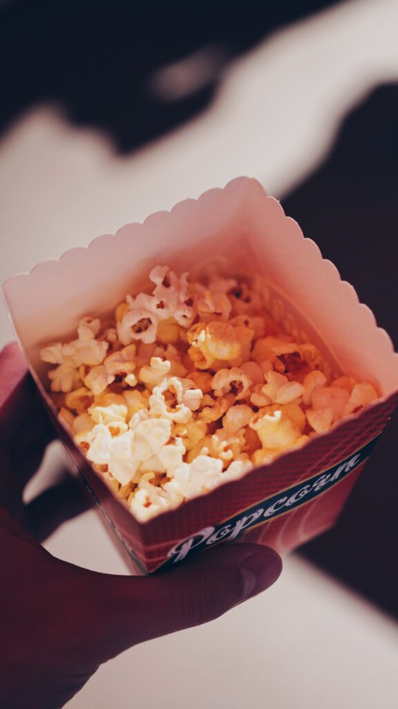 Photo of a paper popcorn bag from above with crunchy popcorn, halved by a shadowy hand, for example at a large event.