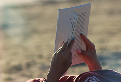 Foto von zwei Händen, die am Strand ein Buch lesen als Symbolbild für Lesetipps.